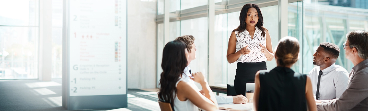 Group of diverse business professionals collaborating with a black woman presenting inside a well lit office.