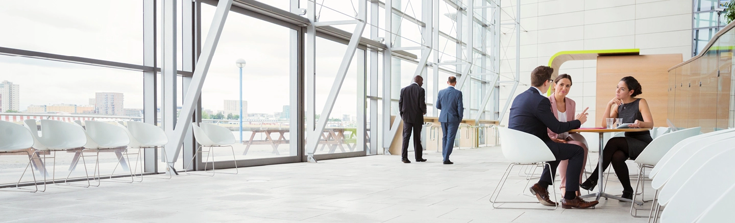 Coleagues in a meeting inside a building with large windows and white chairs.