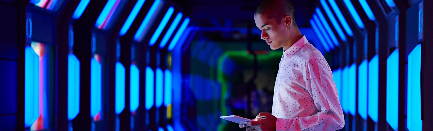 Person with tablet in neon-lit futuristic corridor.