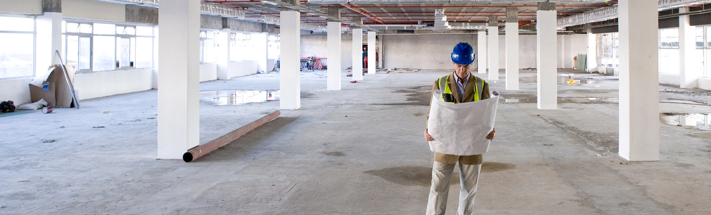 Construction worker reviewing blueprint in unfinished building.