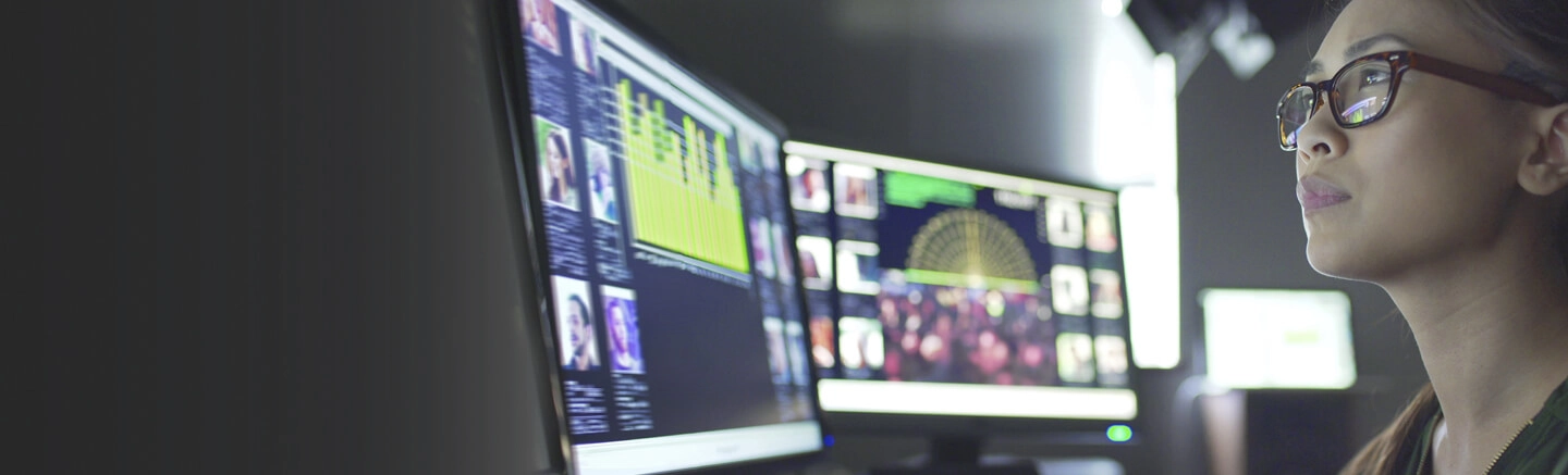 Person at desk with multiple monitors showing charts, graphs, and images; face partially obscured.