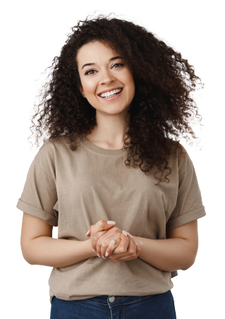 A woman with curly hair smiles with her hands clasped in front of her. She wears a beige shirt and blue jeans,